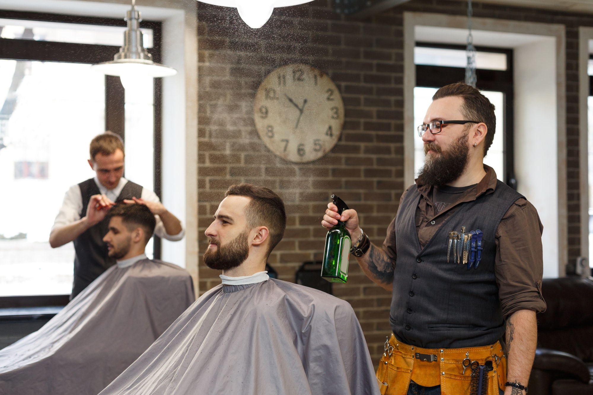 man getting haircut by hairstylist at barbershop